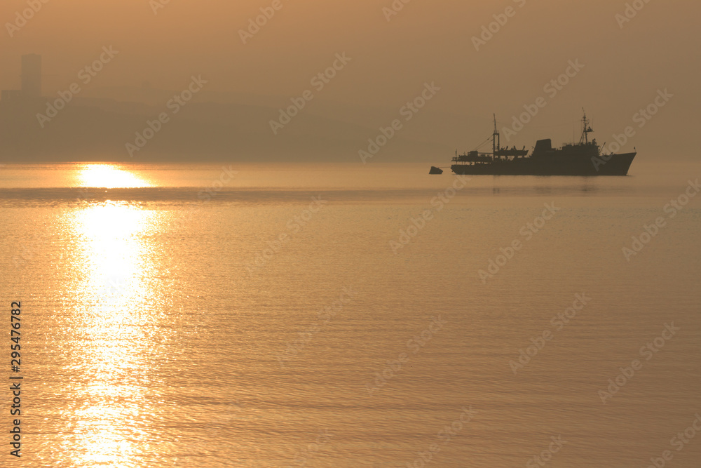 A ship sails into the distance in the early morning fog at dawn.