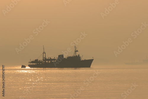 A ship sails into the distance in the early morning fog at dawn.