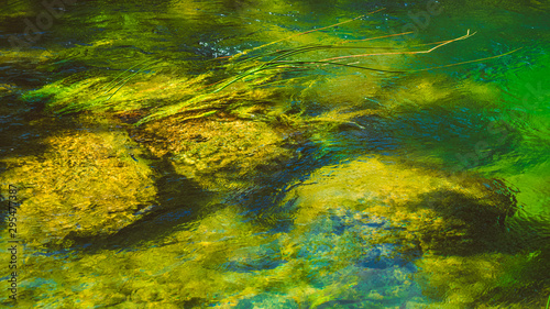 Green, blue and yellow reflections in the river flow. Abstract background