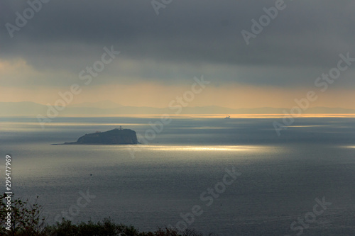 Skrypleva Island, where Vladivostok's oldest lighthouse is located, lit by the sun breaking through thunderclouds. photo