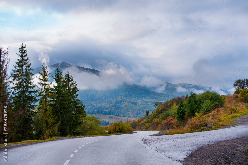 Fototapeta premium Road wet after rain between mountains without cars. This is a countryside, cars and buses rarely travel. Above the mountains are the mist and the cloudy sky