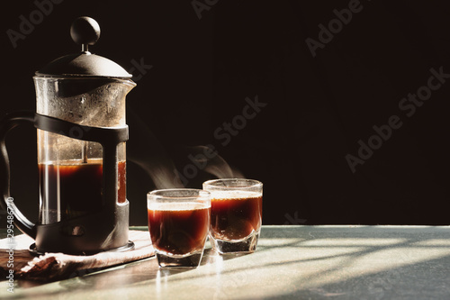 Aromatic coffees with hot smoke are poured into couple cup from French press coffee maker, Hot drink is good for health,On old wood table,Black background,Natural light,Selective focus,Vintage style.