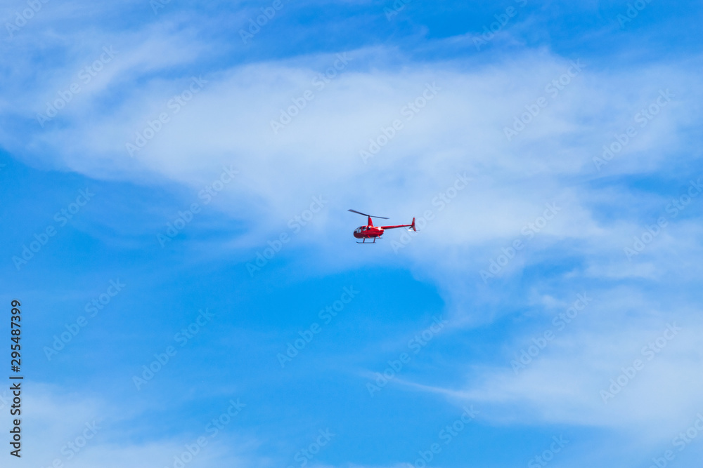 Red helicopter flying in the sky. Small red helicopter in the blue sky Red helicopter flying in the sky. Small red helicopter in the blue sky