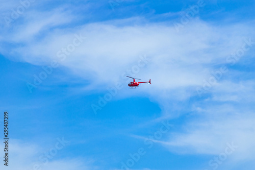 Fototapeta Naklejka Na Ścianę i Meble -  Red helicopter flying in the sky. Small red helicopter in the blue sky