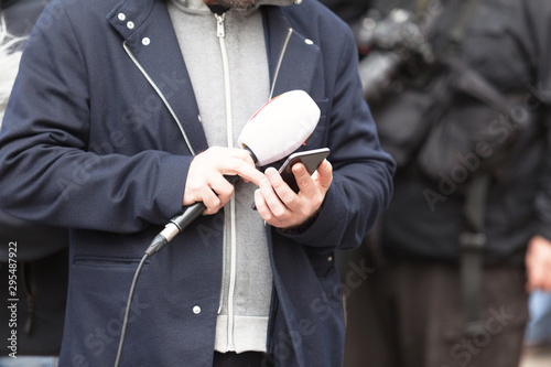 Journalist at media event holding microphone and phone, waiting for news conference © wellphoto