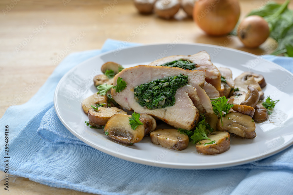 chicken breast fillet stuffed with spinach, served with mushrooms and parsley garnish on a blue napkin and a light wooden table, copy space, selected focus, narrow depth of field chicken breast fillet stuffed with spinach, served with mushrooms and parsley garnish on a blue napkin and a light wooden table, copy space, selected focus, narrow depth of field