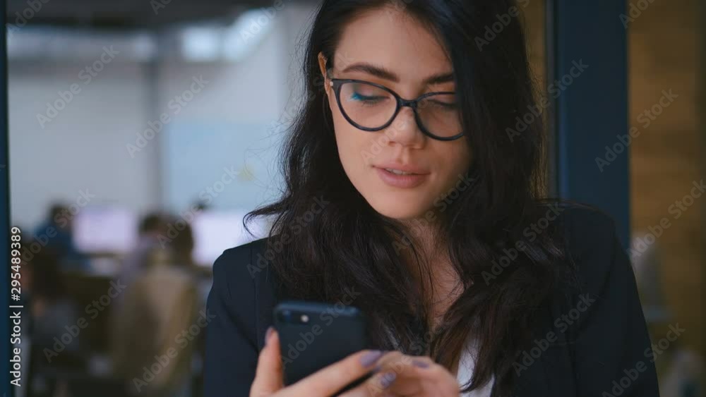 Close-up Portrait of Beautiful Young Woman Using Smartphone in Office. Business Lady in Formal Wear Dress Typing Messages on her Mobile Phone.