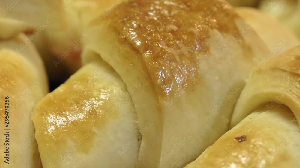 A close up shot of freshly made dinner rolls stuffed with shredded ham and cheese and glazed with egg wash; slow motion. A close up shot of freshly made dinner rolls stuffed with shredded ham and cheese and glazed with egg wash; slow motion.