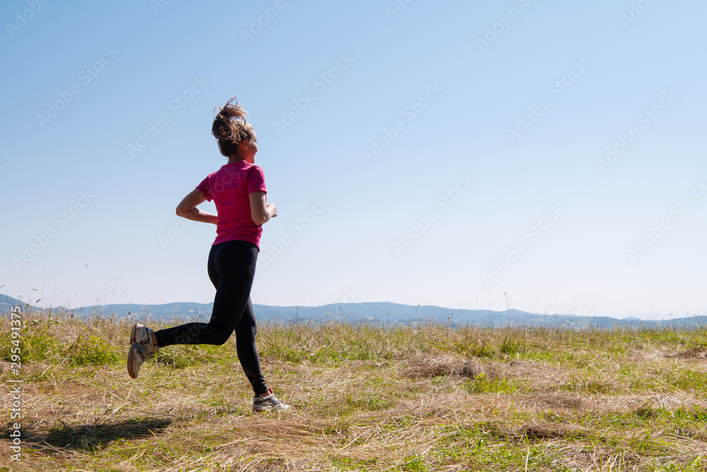 young woman jogging on sunny day at summer mountain