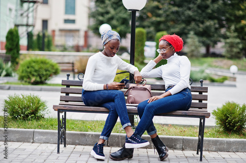Two young modern fashionable, attractive, tall and slim african muslim womans in hijab or turban head scarf posed together with mobile phones at hands.