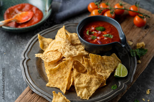 Traditional Mexican appetizers of hot crispy nachos with tomato salsa sauce dip.	