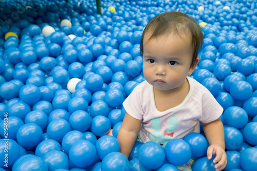 Asian kid in blue ball pond. Baby playing in dry ball pond indoor playground.