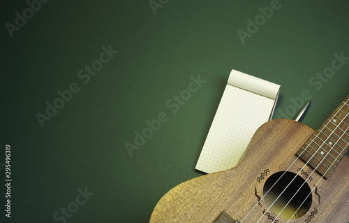 Flat lay a ukulele and a notepad on a green background