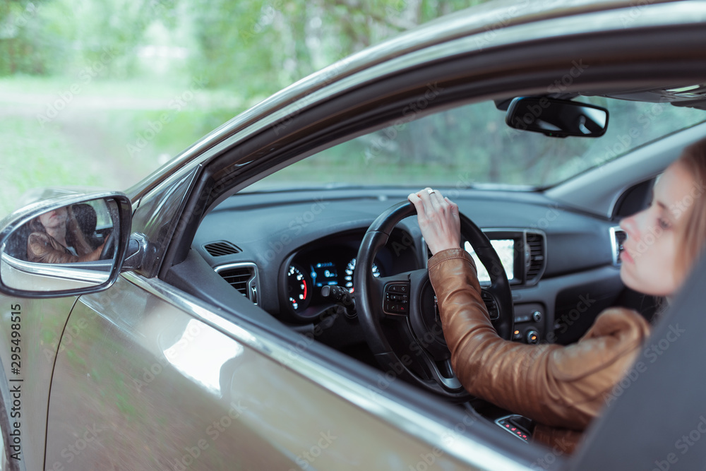 woman driving a car, in summer and autumn outside city in forest, looks in rear view mirror, reversing, parking car, looks out window, gives back.