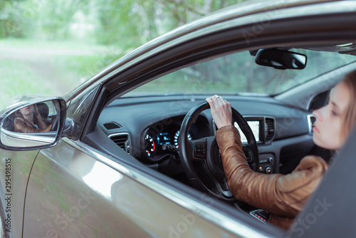 woman driving a car, in summer and autumn outside city in forest, looks in rear view mirror, reversing, parking car, looks out window, gives back.