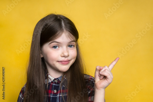cute little  girl  pointing with finger standing against yellow background. 