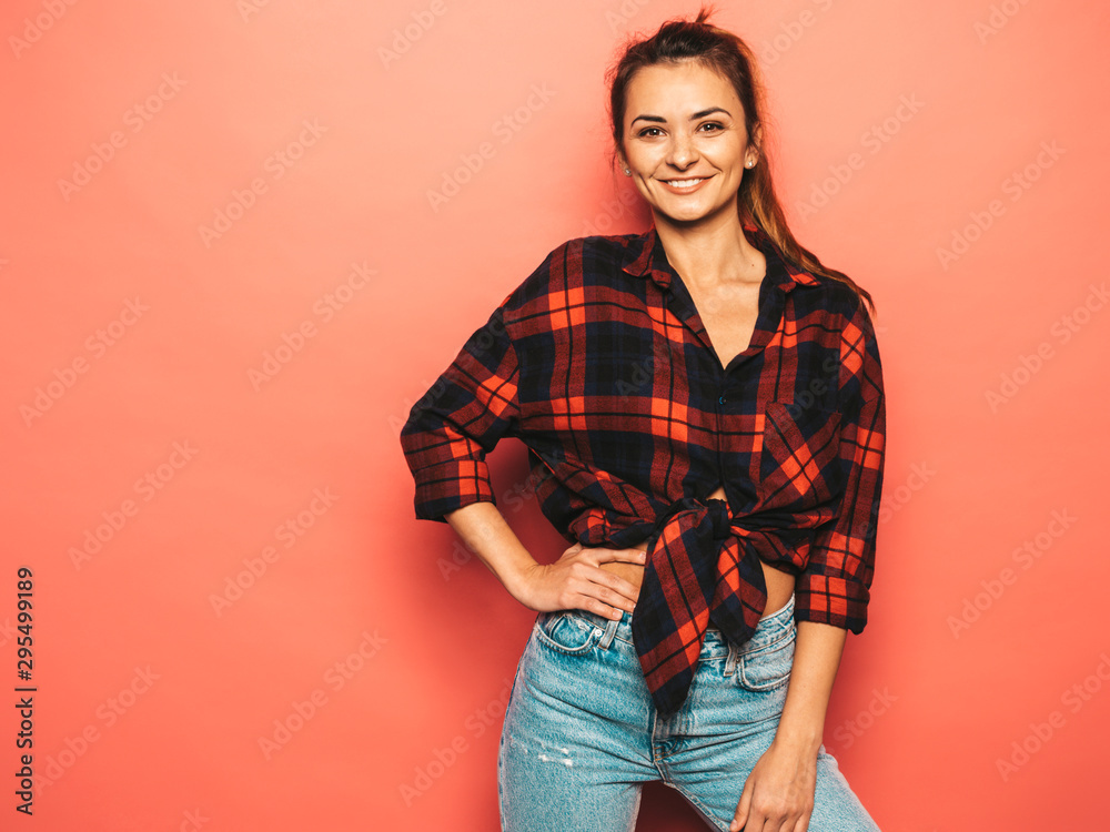 Portrait of young beautiful smiling hipster girl in trendy summer checkered shirt and jeans clothes. Sexy carefree woman posing near pink wall in studio. Positive model with no makeup. Portrait of young beautiful smiling hipster girl in trendy summer checkered shirt and jeans clothes. Sexy carefree woman posing near pink wall in studio. Positive model with no makeup.