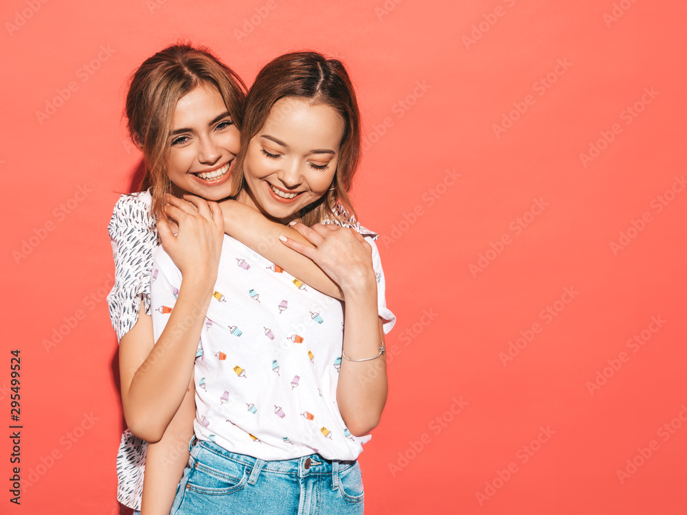 Two young beautiful smiling blond hipster girls in trendy summer colorful T-shirt clothes. Sexy carefree women posing near blue wall. Positive models having fun.Hugging Two young beautiful smiling blond hipster girls in trendy summer colorful T-shirt clothes. Sexy carefree women posing near blue wall. Positive models having fun.Hugging