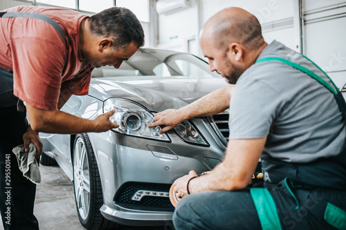 Two professional workers talking and checking car details during valeting and polishing procedure.