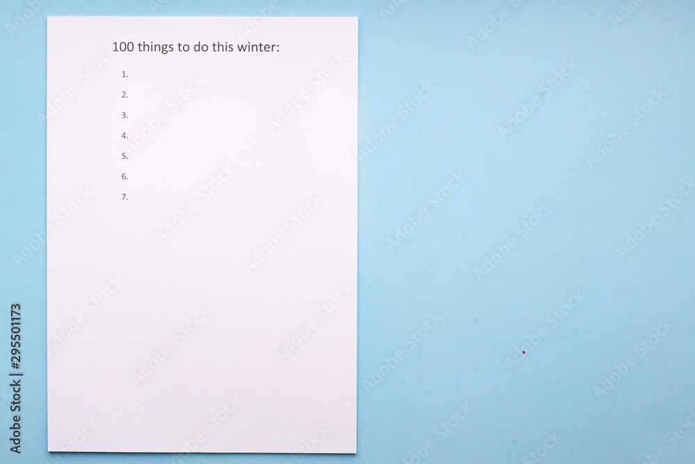 Caption 100 things to do this winter on white sheet. White sheet on a blue background. Travel planning. Caption 100 things to do this winter on white sheet. White sheet on a blue background. Travel planning.