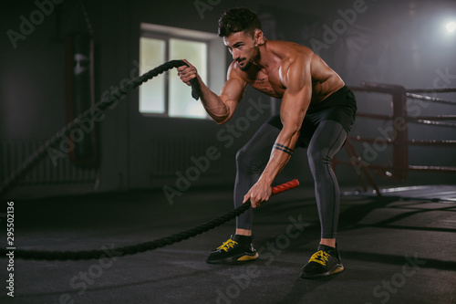 Hard exercises with ropes athletic man practicing cross fit training he make concentrated face while doing his workout