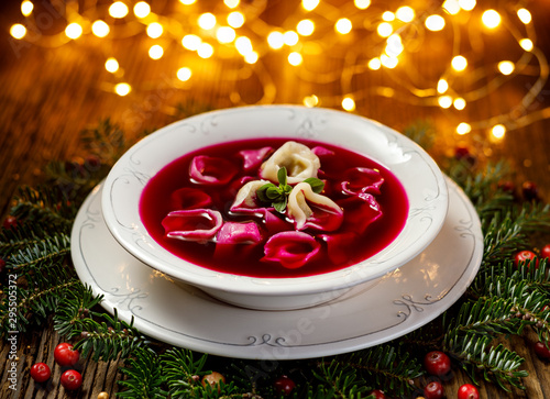 Christmas beetroot soup, red borscht with small dumplings with mushroom filling in a ceramic white plate on a wooden table.Traditional Christmas eve dish in Poland.  photo