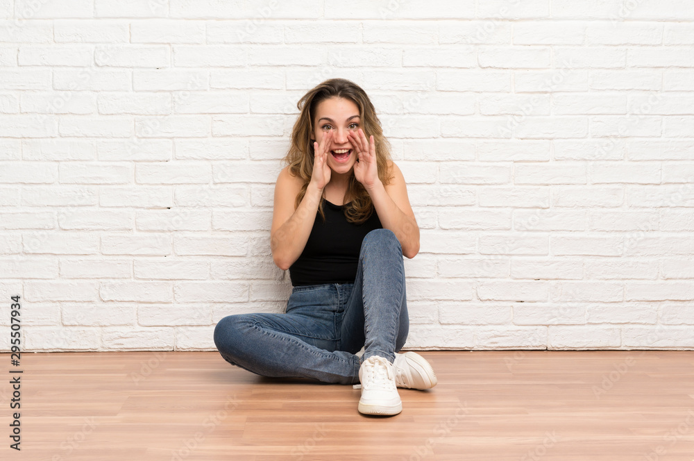 Young blonde woman sitting on the floor shouting with mouth wide open Young blonde woman sitting on the floor shouting with mouth wide open