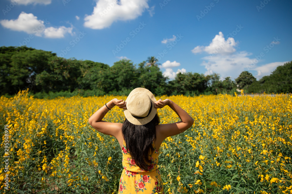 Asian woman traveler with backpack holding hat and looking at  flowers farm with blue sky