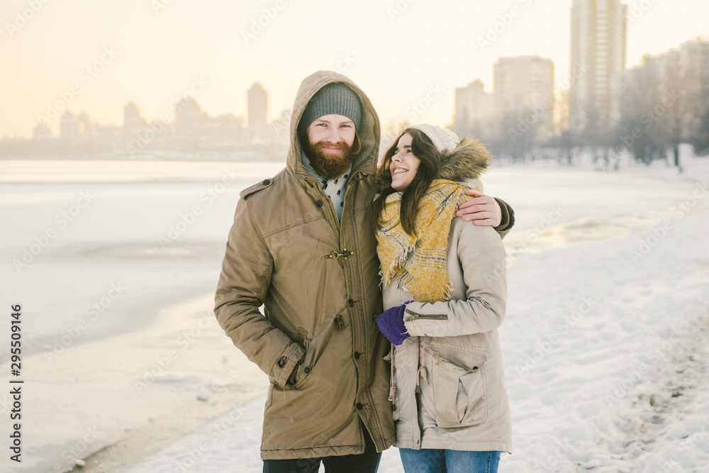 Theme love and date on nature. A young Caucasian heterosexual couple guy and girl walk in the winter along a frozen lake in winter. Bearded Man Hugging Woman. Valentine's day holiday Theme love and date on nature. A young Caucasian heterosexual couple guy and girl walk in the winter along a frozen lake in winter. Bearded Man Hugging Woman. Valentine's day holiday