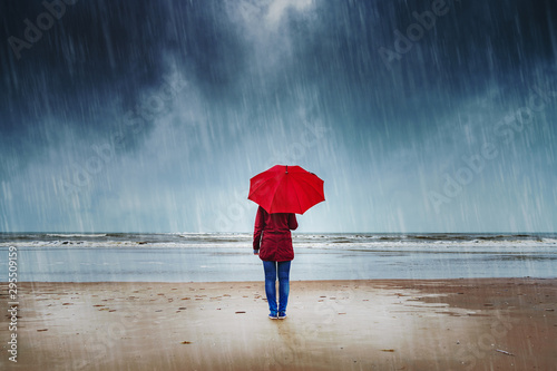 Fototapeta Lonely woman with red umbrella is standing in the rain watching the sea