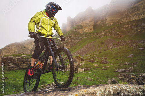 Fototapeta Naklejka Na Ścianę i Meble -  Side view wide angle partly a man on a mountain bike travels on rocky terrain Against the background of cloudy sky and epic rocks. The concept of a mountain bike and mtb downhill