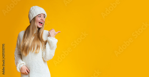 Cheerful girl pointing with thumb at empty space photo