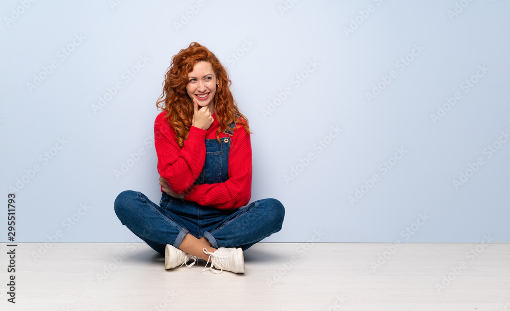 Redhead woman with overalls sitting on the floor looking to the side Redhead woman with overalls sitting on the floor looking to the side