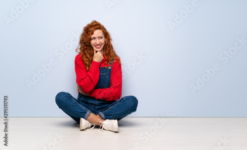 Redhead woman with overalls sitting on the floor looking to the side