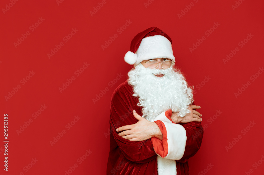 Santa Claus freezes, warms up against a red background and looks in camera with a sad face.Portrait Santa Claus who is cold. Man in santa costume freezing on red background. Cold winter for Christmas Santa Claus freezes, warms up against a red background and looks in camera with a sad face.Portrait Santa Claus who is cold. Man in santa costume freezing on red background. Cold winter for Christmas