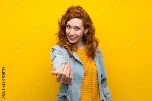 Redhead woman over isolated yellow background inviting to come
