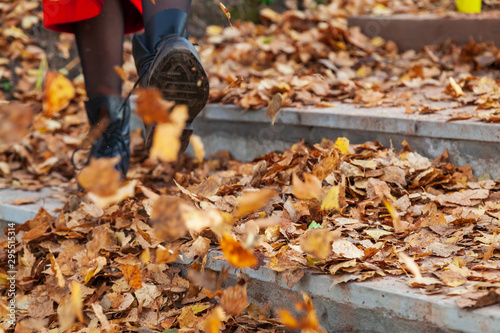 A girl in black boots and a red coat kicks yellow and red foliage strolling in the park alone on a clear autumn day during a fall. Freshness, nature and fun.