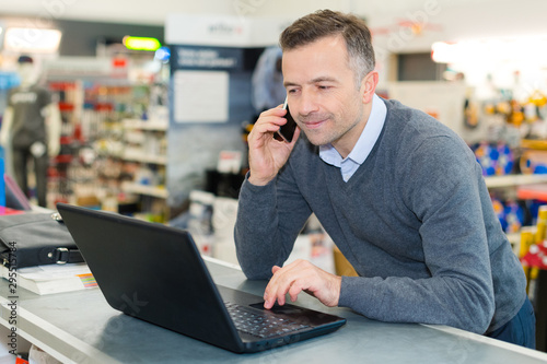salesman talking on smartphone while looking at laptop photo