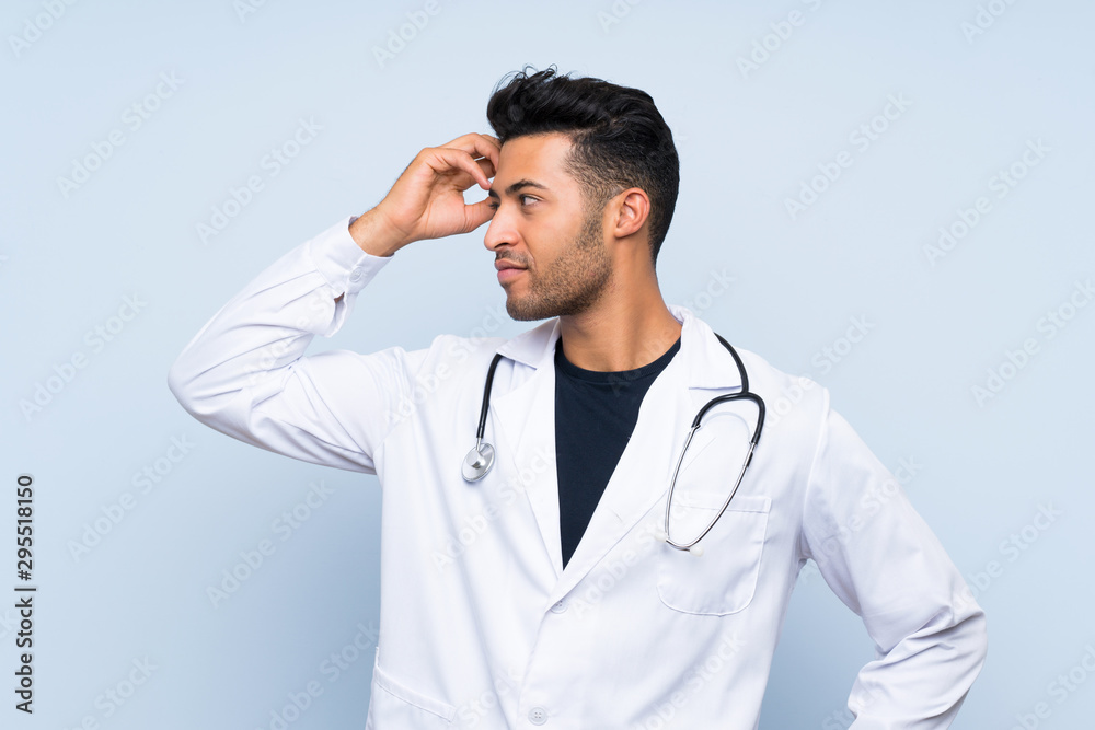 Young doctor man over isolated blue wall having doubts and with confuse face expression Young doctor man over isolated blue wall having doubts and with confuse face expression