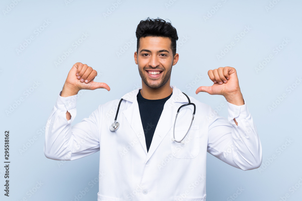 Young doctor man over isolated blue wall proud and self-satisfied Young doctor man over isolated blue wall proud and self-satisfied
