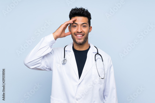 Young doctor man over isolated blue wall with surprise and shocked facial expression