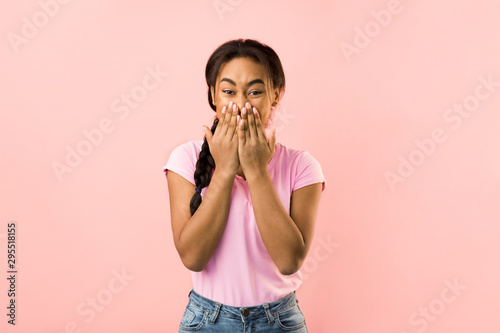 Shocked woman covering her mouth with hands, pink background