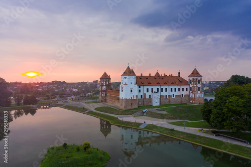 Mirsky Castle and its reflection in the lake in summer. Sunset in cloudy weather with rain clouds.