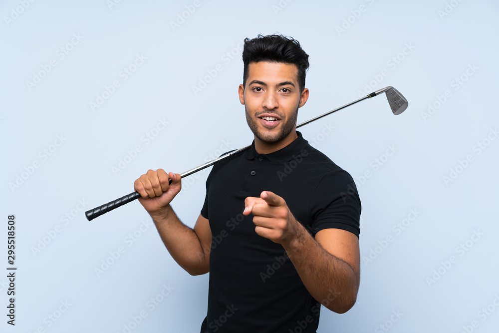 Handsome young man playing golf over isolated blue background surprised and pointing front Handsome young man playing golf over isolated blue background surprised and pointing front