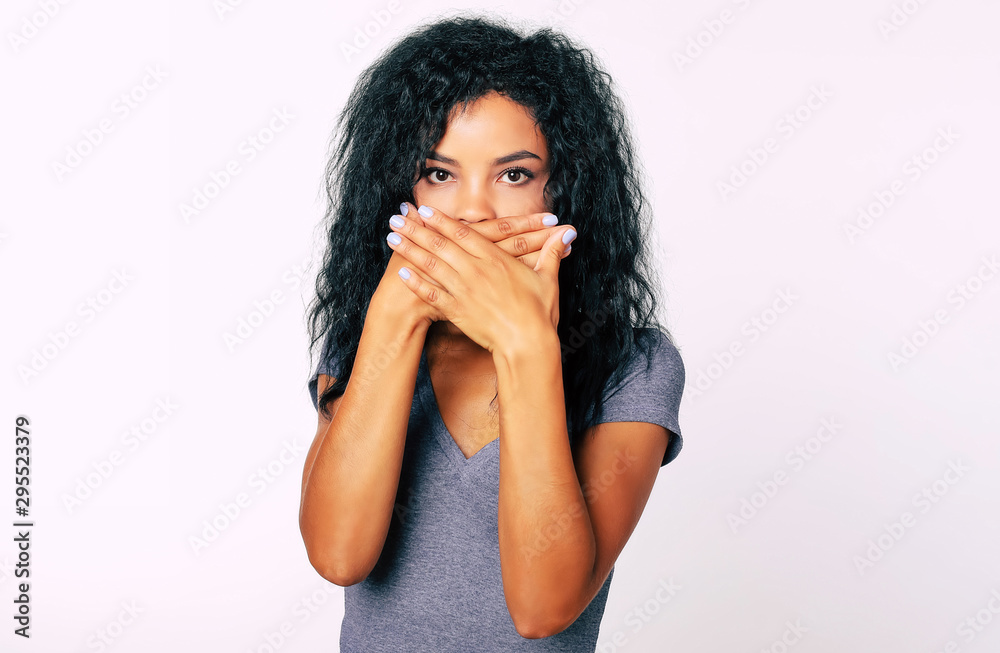 Silence is golden. Front portrait of worried or shocked Afro woman with bushy jet-black hair and wide eyes looking at the camera standing with palms covering her mouth. Silence is golden. Front portrait of worried or shocked Afro woman with bushy jet-black hair and wide eyes looking at the camera standing with palms covering her mouth.