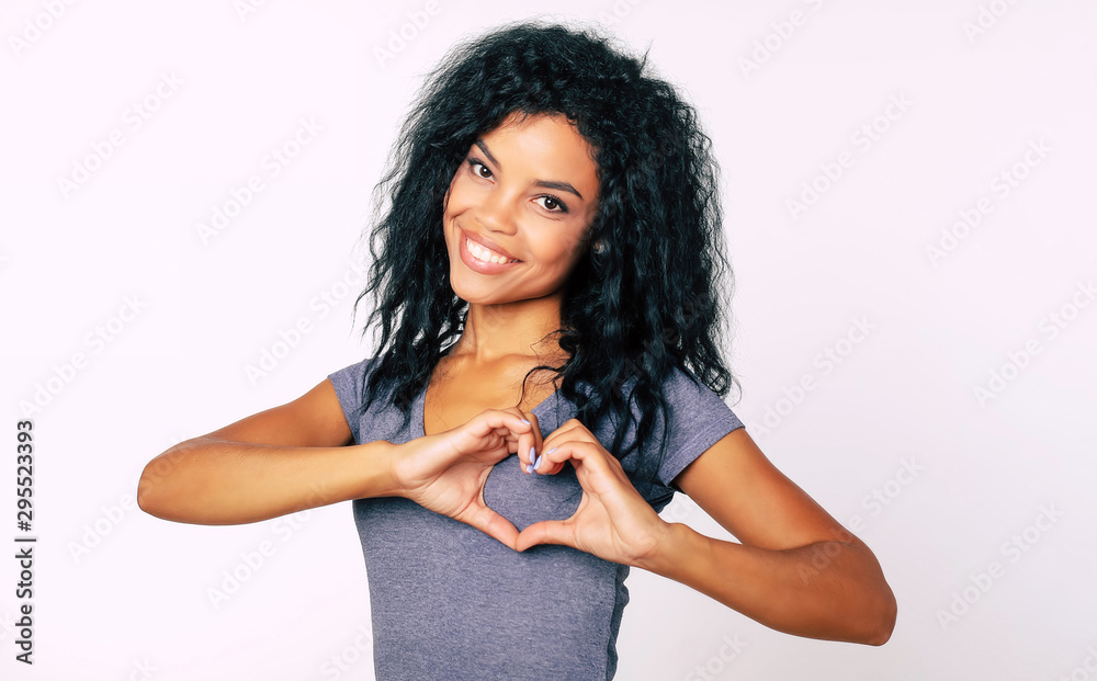 Thank you! Close-up portrait of content Afro ethnic girl with messy raven black hair standing smiling broadly, with her palms near her chest showing a hand heart. Thank you! Close-up portrait of content Afro ethnic girl with messy raven black hair standing smiling broadly, with her palms near her chest showing a hand heart.