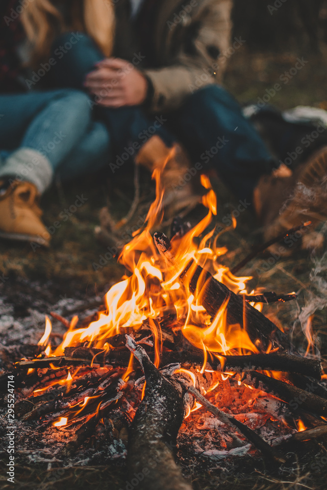 Traveler couple camping in the forest and relaxing near campfire after a hard day. Concept of trekking, adventure and seasonal vacation. - obrazy, fototapety, plakaty 