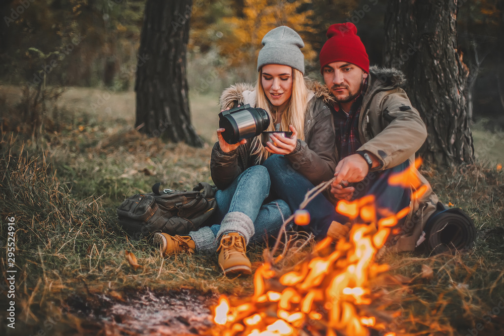 Traveler couple camping and roasting marshmallows over the fire in the forest after a hard day. Concept of trekking, adventure and seasonal vacation.