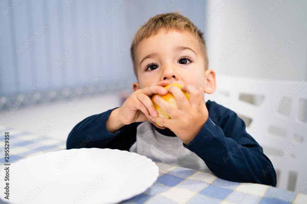 Portrait of small little boy three years old eating an apple fruit by the table at home Portrait of small little boy three years old eating an apple fruit by the table at home