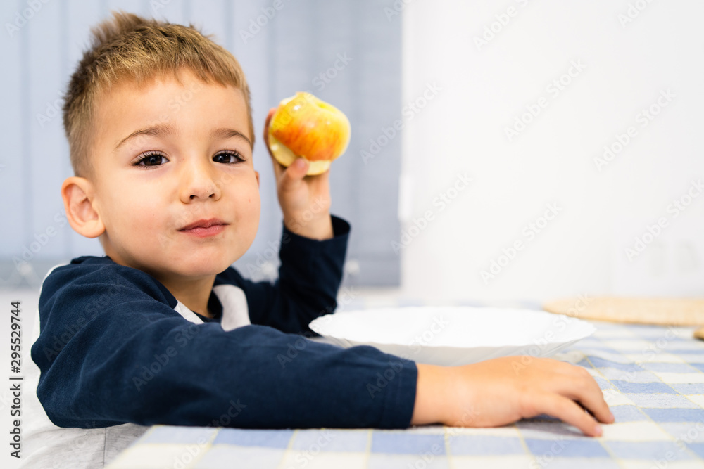 Portrait of small little boy three years old eating an apple fruit by the table at home Portrait of small little boy three years old eating an apple fruit by the table at home